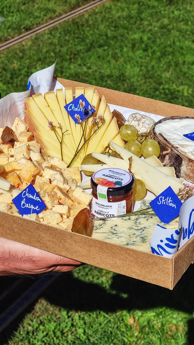Un plateau de fromages tenu à deux mains dans un jardin.