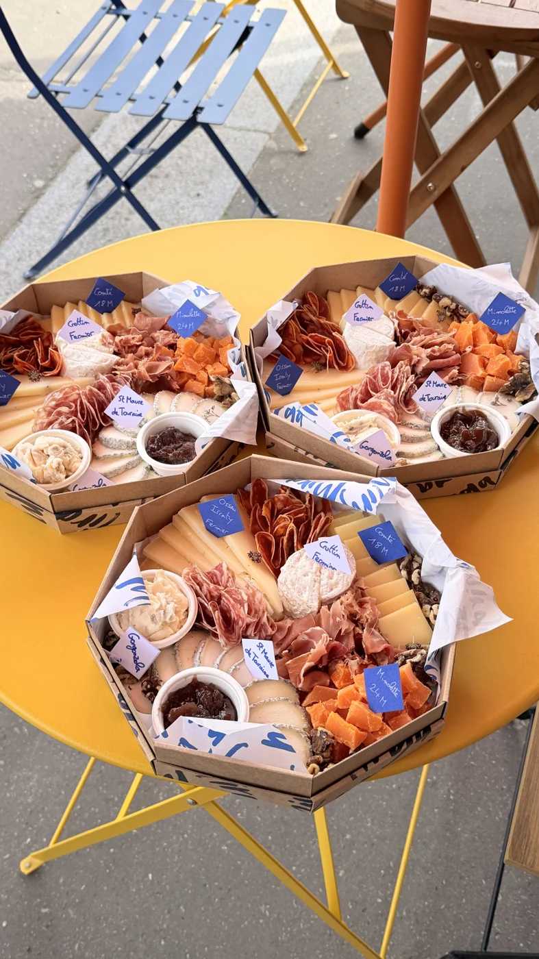 Trois plateaux octogonaux de fromages et charcuterie sur une table jaune.