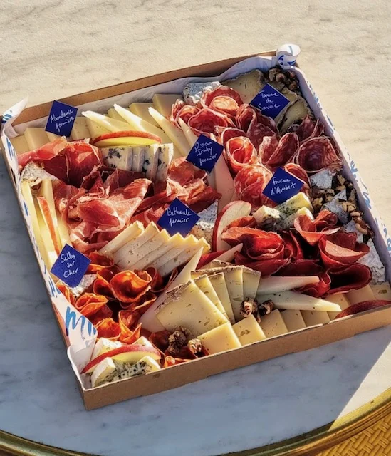 Un plateau carré composé de fromages et de charcuteries, en lumière naturelle.